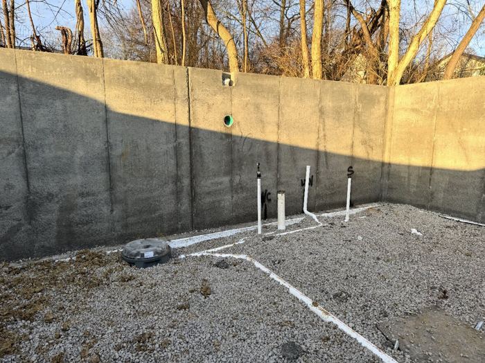 Underground plumbing rough-in inside a poured foundation, with capped stub-ups and a floor drain set in gravel ready for the slab